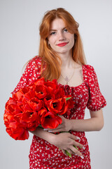 Young happy woman with a bouquet of red lulips. Portrait of a red-haired lady in the studio in front of a white background.