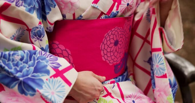 Woman, japanese and hands with belt for kimono, fashion tradition or style on park bench. Closeup, female person or waist with fabric, material or japan clothing for culture, dress or asian heritage