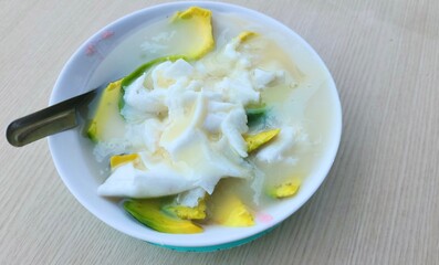Es Oyen in a white bowl on a table is a popular drink from the city of Bandung filled with several fruits such as avocado, young coconut,and sago pearls, jelly,then mixed with sweetened condensed milk