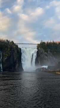 Montmorency Falls near Quebec City, Canada, cascading dramatically from a height of 83 meters with a suspension bridge above, surrounded by autumnal foliage and misty skies