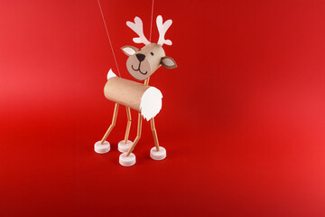 Handmade reindeer craft, cardboard tube body, straw stick legs, plastic bottle cap hooves, paper antlers, red background, festive DIY holiday decoration, creative use of everyday materials
