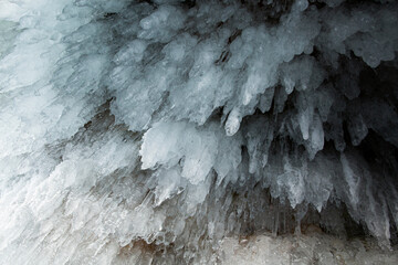 View from the ice cave on Lake Baikal. Many beautiful icicles on the walls and ceiling. Thick and thin icicles. Ice on the floor.