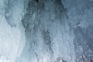 View from the ice cave on Lake Baikal. Many beautiful icicles on the walls and ceiling. Thick and thin icicles. Ice on the floor.