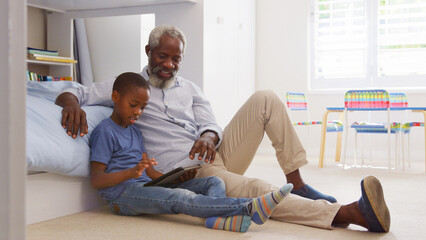 Obraz premium Grandfather Sitting With Grandson In Child's Bedroom Using Digital Tablet Together