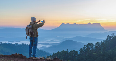 Male Hiker with backpack using smartphone taking photos mountains landscape. Sharing travel lifestyle and adventure vacations. Use outdoor modern technology