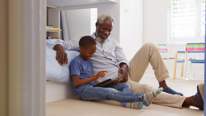 Grandfather Sitting With Grandson In Child's Bedroom Using Digital Tablet Together