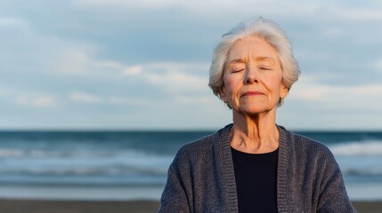 An elderly woman stands peacefully at the beach, eyes closed, enjoying the tranquility of the waves and the serene atmosphere around her.
