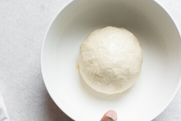 Overhead view of challah dough being shaped in white bowl, top view of homemade challah bread dough, process of making challah