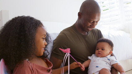 Father And Daughter Dressed As Fairy Sitting In Bedroom Playing With Baby Brother