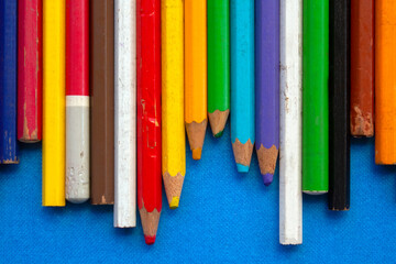 close up of colored wooden pencils in a row, on blue background. top view