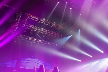 Lighting equipment under roof of concert hall. Bright spotlights shine onto stage from above. Lighting equipment on metal structures. Spotlights for concert. Spotlight beams among purple neon light