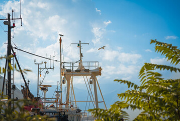 Nautical equipment and seagulls frame the boats mast, with the open sky and clouds capturing a serene coastal atmosphere.