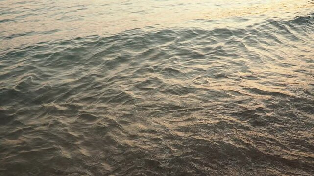 Waves gently lap at shore during stunning sunset over ocean. Golden sunlight reflects off waves as they roll onto shore, creating tranquil atmosphere at sunset by sea. Montenegro summer, Canj