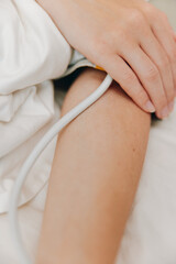 Person laying in bed with blood pressure cuff on arm, another person holding arm up with cuff on it