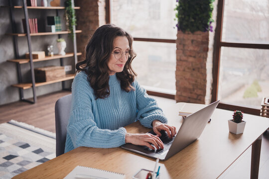 Mature woman joyfully engages in laptop work inside a brightly lit home office setting