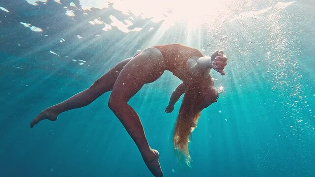 Teen girl in red suit swims underwater in the sea. Relaxed teen girl dives and swims underwater. Girl dances underwater