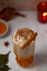 Autumnal spiced pumpkin latte with whipped cream, cinnamon and maple sirup with leaves and candles on background. Halloween or Thanksgiving drink for single serving. Coffee as a dessert
