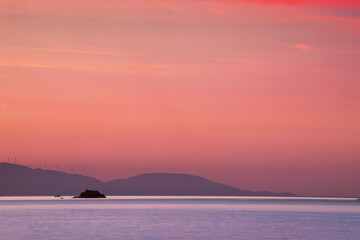 Breathtaking pink and purple sunset over calm ocean with small island and distant hills