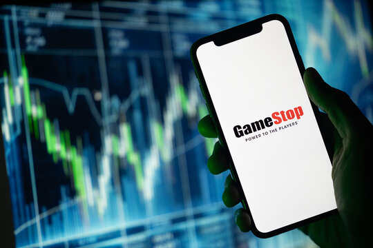In silhouette, a hand holds a mobile phone with the GameStop logo displayed. Behind it, a backdrop illustrates ascending stock prices highlighted in green color