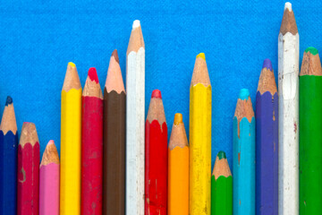 close up of colored wooden pencils in a row, on blue background. top view