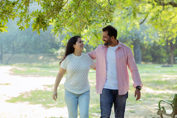 Obraz premium Joyful Walk: A Couple Enjoying a Peaceful Moment Together,A candid photograph of a happy couple walking arm in arm through a lush green park.