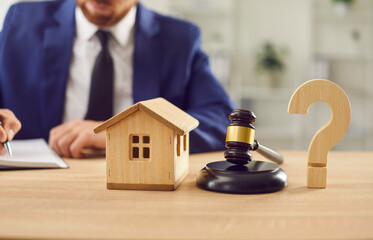 Judge gavel, small wooden toy house and a question mark standing at the desk with a male lawyer...