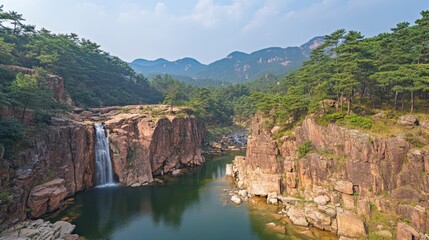 Fototapeta premium Serene Waterfall Cascading into a Clear River Surrounded by Lush Green Forest and Majestic Mountains Under a Bright Blue Sky