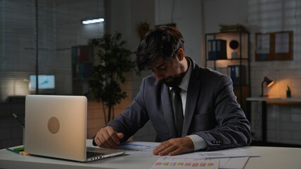 Adult business man manager sitting at desk working on laptop in office, holding hands on the table, upset expression, disappointed gesture.