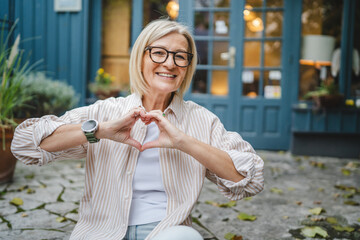 portrait of mature woman sit connect fingers show heart symbol