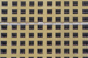 New residential building with a yellow facade and empty windows, highlighting ongoing construction in a busy urban setting