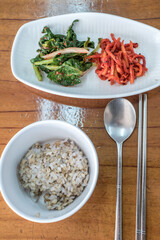 Korean Barley Rice Bowl with Banchan and Traditional Utensils on Wooden Table