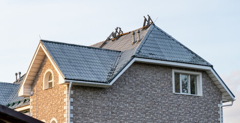Workers are repairing the roof of a modern house with a textured facade during daylight hours, highlighting the need for home upkeep and safety