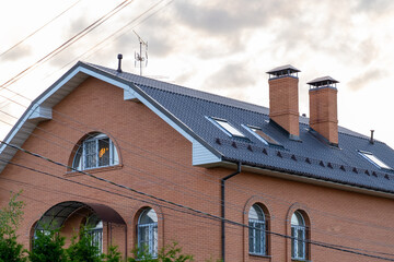 A striking brick house features distinctive rooflines and windows, set against a backdrop of soft clouds during the late afternoon hours