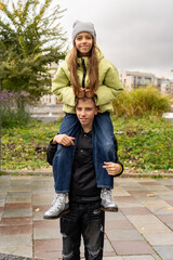 A boy gives a girl a piggyback ride in a park, showcasing joy and friendship against a backdrop of...
