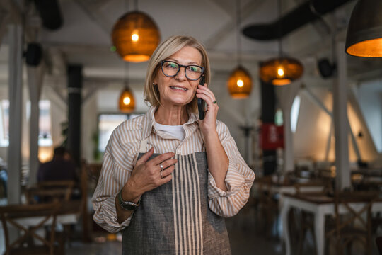mature woman waitress stand at restaurant and talk on mobile phone