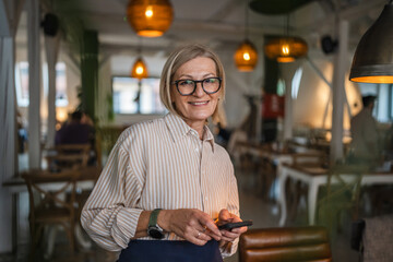 mature woman waitress stand at restaurant and use cellphone