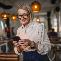 mature woman waitress stand at restaurant and use cellphone
