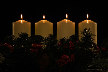 Four white advent candles, all are lit, with garland below on a black background