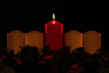 four white advent candles in a row, with a red lit Christ candle in the center, and garland below. 