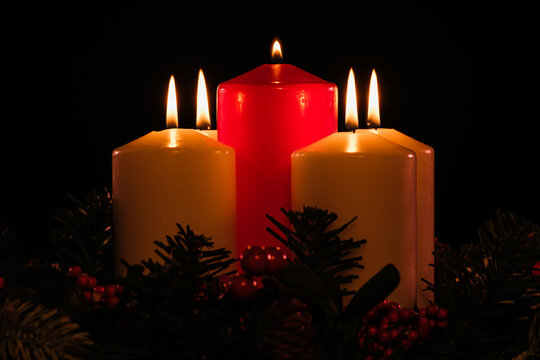 four lit white advent candles with a lit red christ candle in the center from a low angle