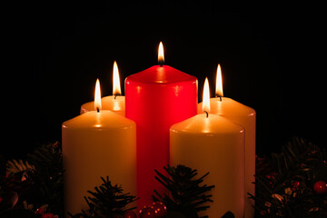 four lit white advent candles with a lit red christ candle in the center from a high angle