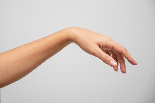 Close-up of an elegant female hand with neutral nail polish against a plain background, showcasing graceful fingers and smooth skin.