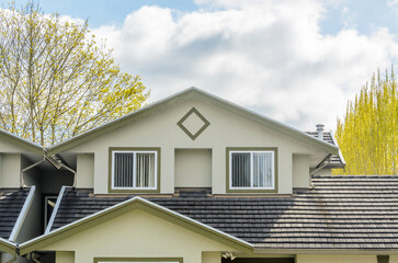 Top of grey stucco luxury house with shingle roof, red and yellow trees and nice windows in Summer in Vancouver, Canada, North America. Day time on June 2024.