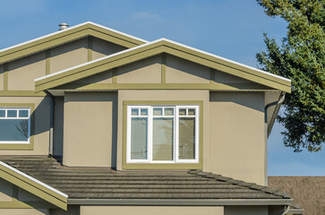 Top of grey stucco luxury house with shingle roof, red and yellow trees and nice windows in Summer in Vancouver, Canada, North America. Day time on June 2024.