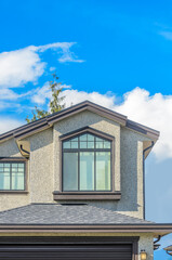 Top of grey stucco luxury house with shingle roof, red and yellow trees and nice windows in Summer in Vancouver, Canada, North America. Day time on June 2024.