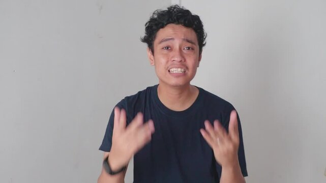 Man Explaining and rejected Gestures. A man stands indoors in front of a white wall, talking and gesturing with his hands.