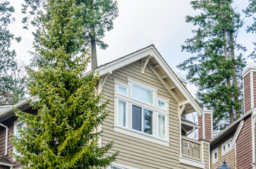 Top of grey stucco luxury house with shingle roof, red and yellow trees and nice windows in Summer in Vancouver, Canada, North America. Day time on June 2024.