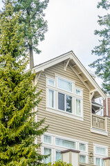 Top of grey stucco luxury house with shingle roof, red and yellow trees and nice windows in Summer in Vancouver, Canada, North America. Day time on June 2024.