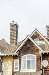 Top of grey stucco luxury house with shingle roof, red and yellow trees and nice windows in Summer in Vancouver, Canada, North America. Day time on June 2024.