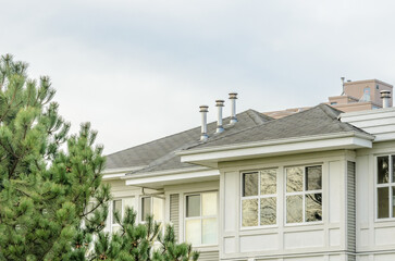 Top of grey stucco luxury house with shingle roof, red and yellow trees and nice windows in Summer in Vancouver, Canada, North America. Day time on June 2024.